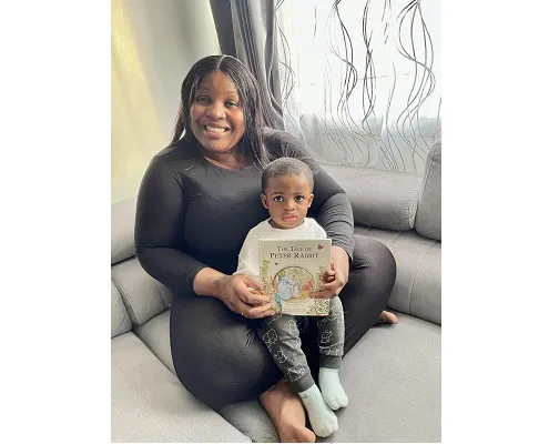 A black woman and her toddler son sitting on a couch next to a window