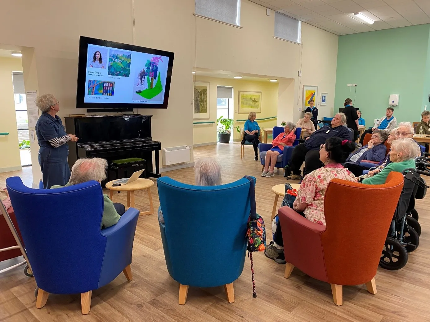 tenants in a communal area gathered round a plasma screen on the wall looking at art