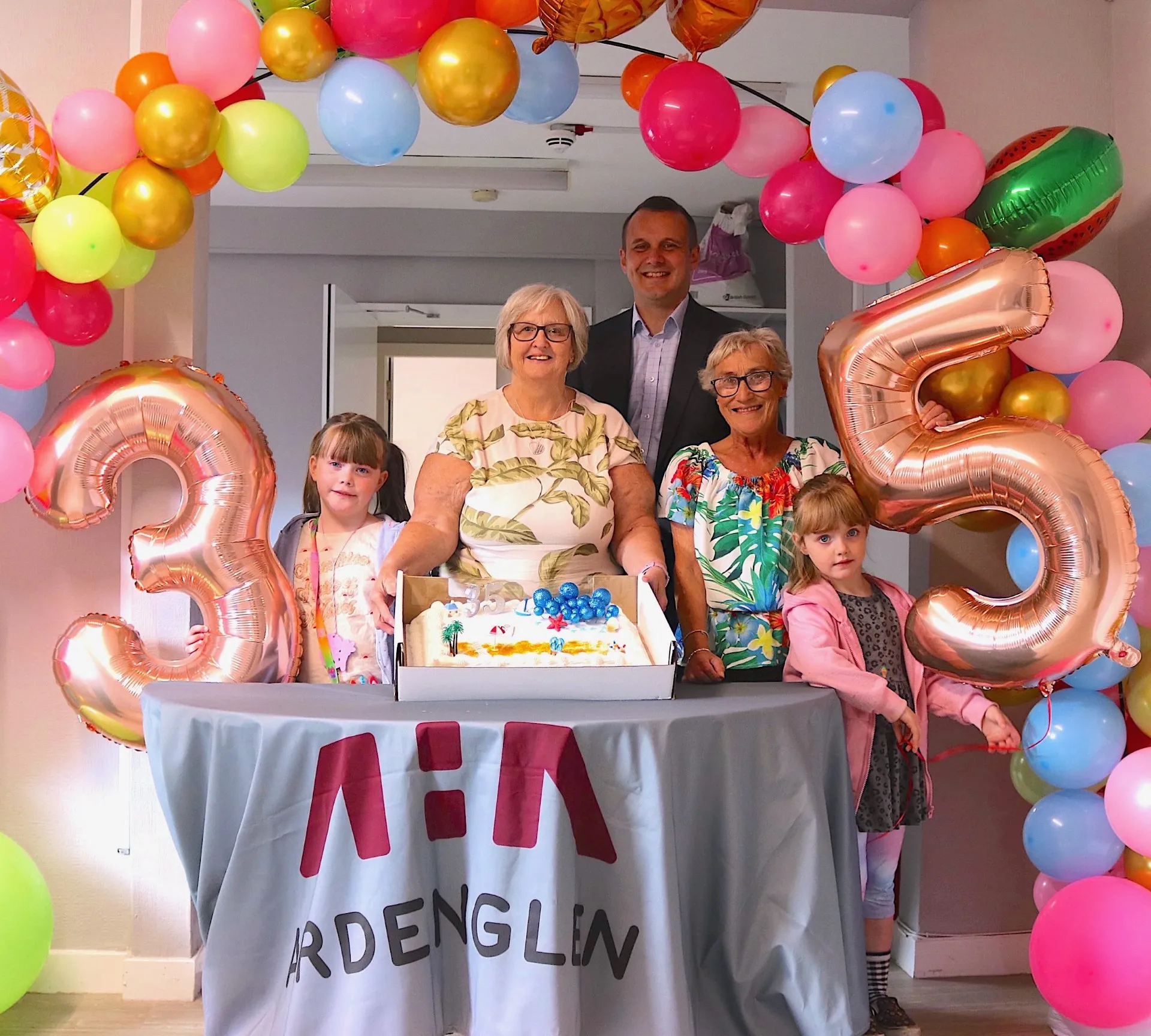 Ardenglen Housing Association staff and a tenant with a child surrounded by celebratory balloons
