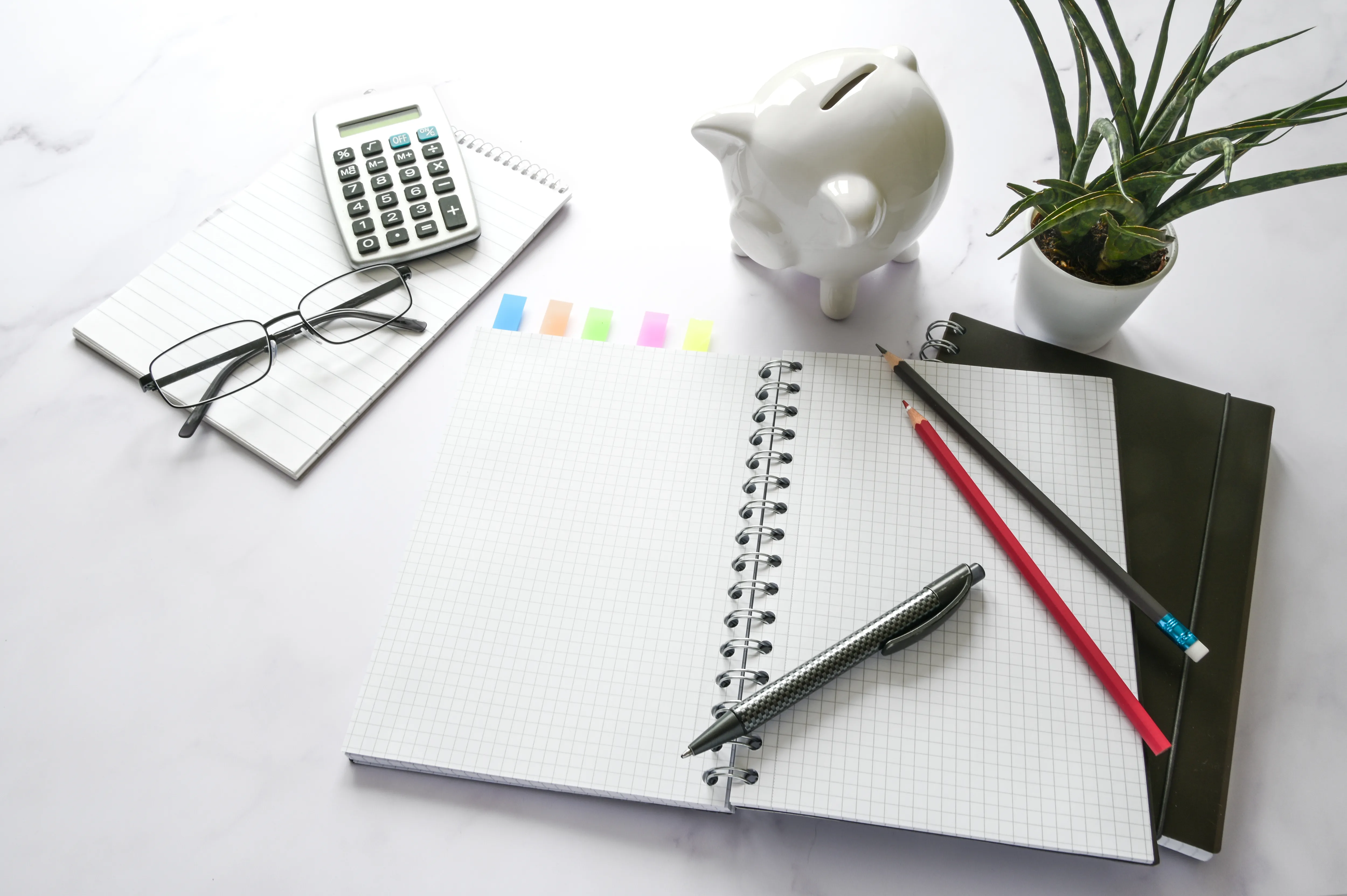table with notepad, piggy bank, pens, glasses and a calculator